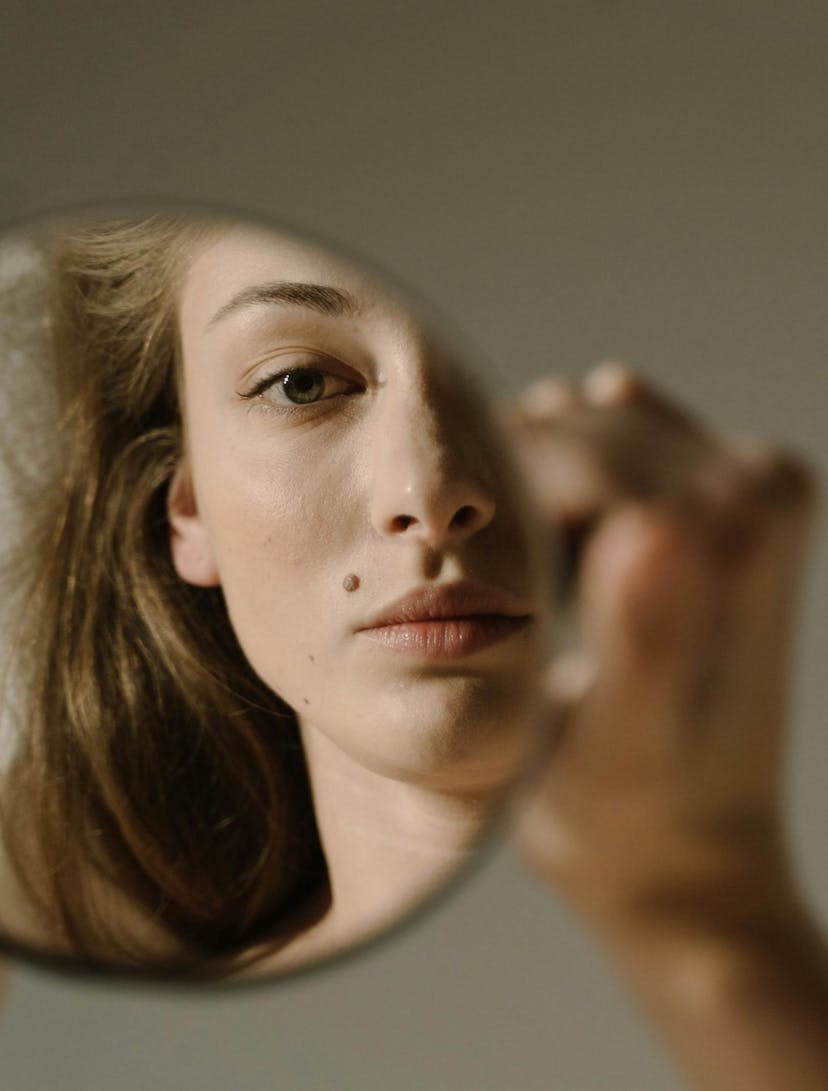 Woman looking at her reflection in the mirror with bags under eyes.