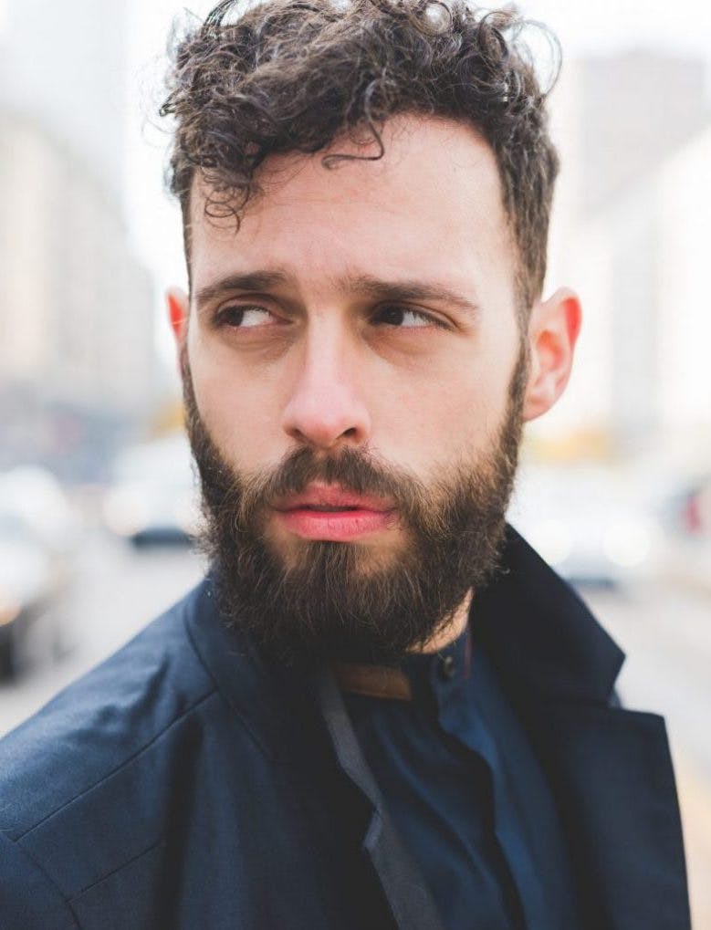 Portrait of young handsome caucasian bearded businessman posing outdoor in the street, overlooking pensive - business, thoughtful, serious concept
