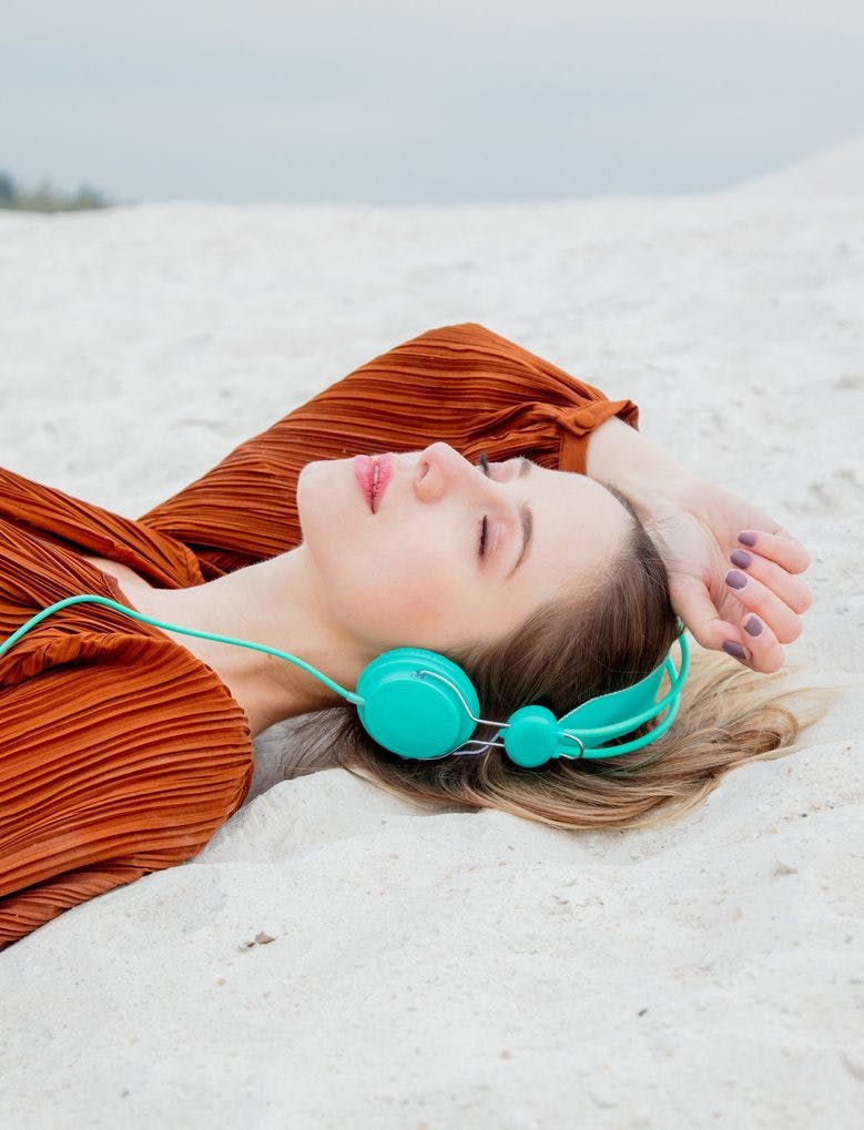 blonde woman on a beach listening to podcast to reduce stress